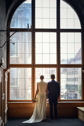 Brautpaar an einem großen Rundbogenfenster mit Stadtblick