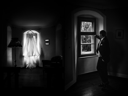 Getting Ready: Brautkleid hängt am Fenster, Bräutigam im abgedunkelten Raum