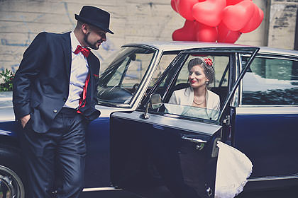 Bräutigam mit Zylinder am Oldtimer, Braut im Wagen