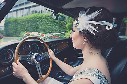 Braut am Steuer eines Oldtimers mit Federhaarschmuck