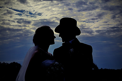 Brautpaar mit Hüten als Silhouette vor dramatischem Himmel