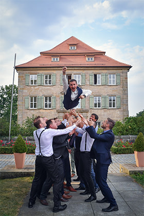 Trauzeugen werfen den Bräutigam vor dem Schloss in die Luft