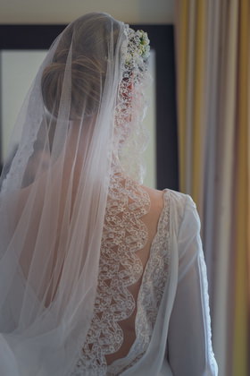 Braut mit Schleier und Spitzenkleid am Fenster von hinten