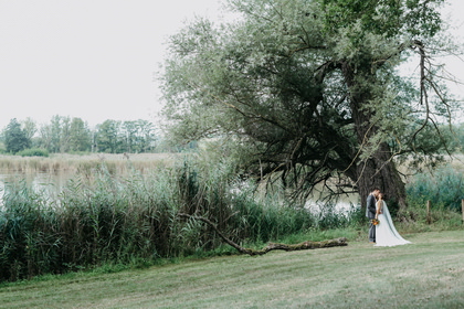 Brautpaar in weiter Landschaft an einem Weiher mit altem Baum