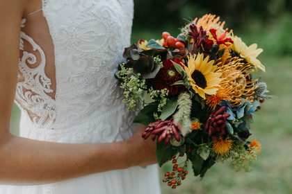 Braut mit buntem Herbststrauß mit Sonnenblume, Detail des Spitzenkleids